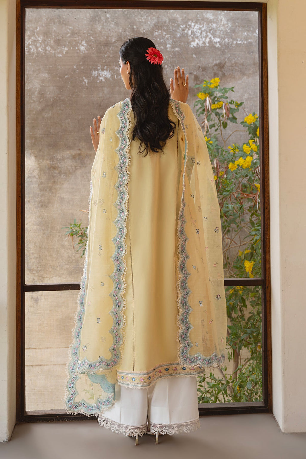 Woman in a yellow traditional outfit standing in front of a decorative mirror with floral patterns.