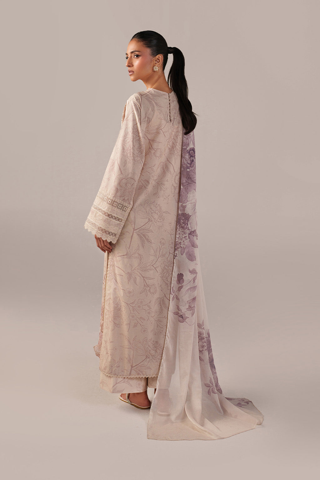 Woman wearing a long, light-colored dress with floral patterns on a plain background