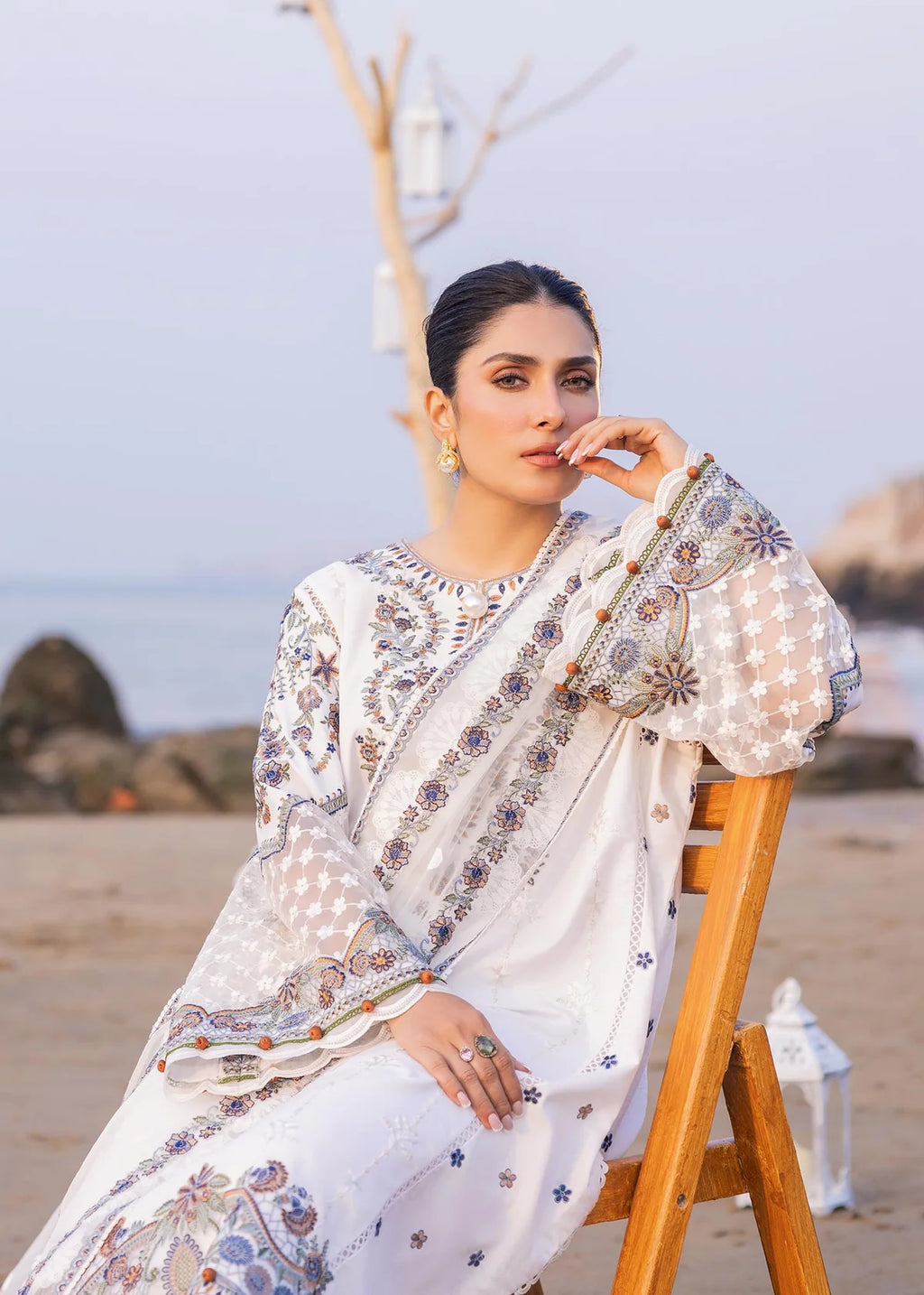 Woman in a patterned outfit sitting on a wooden chair by the beach.