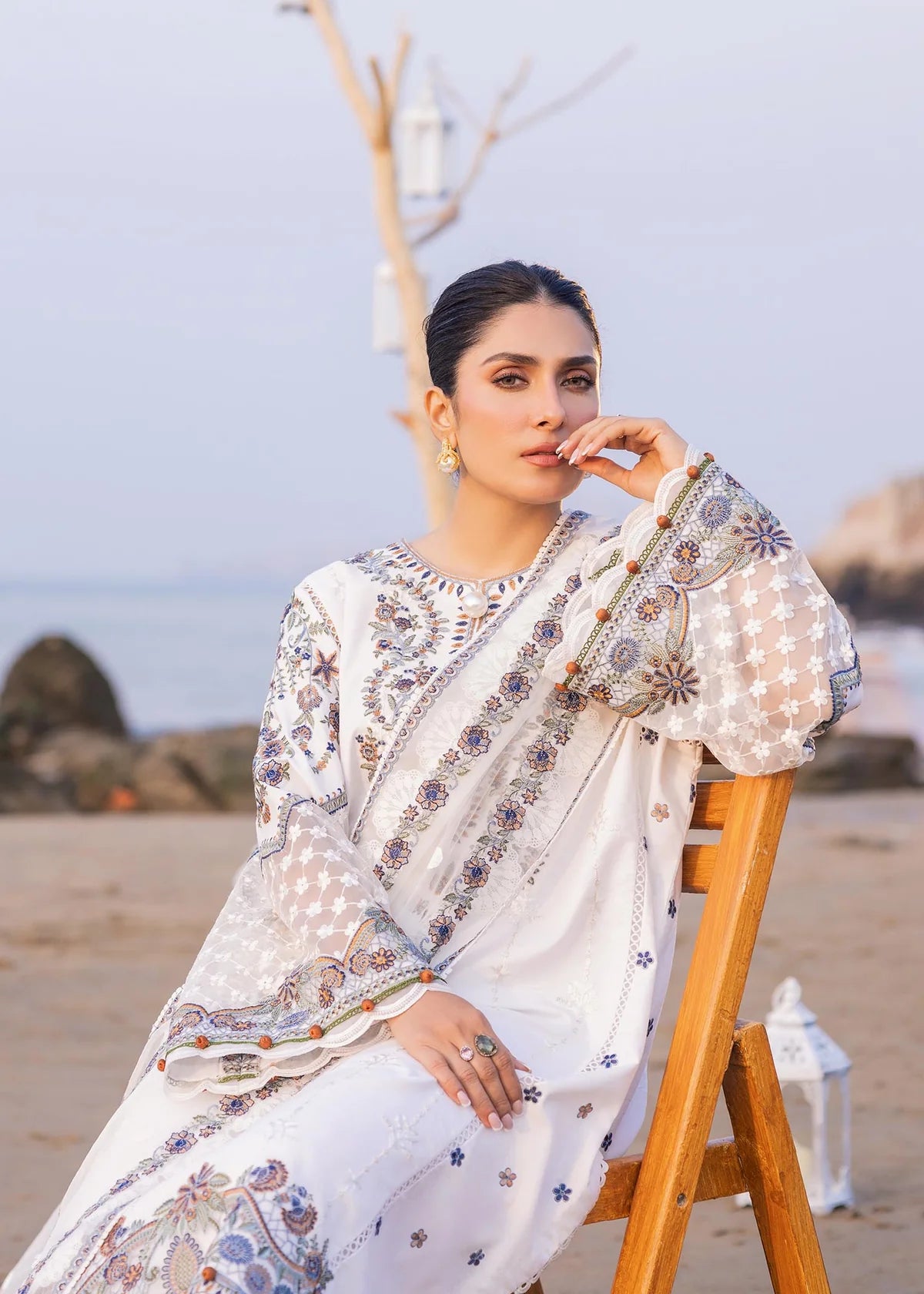 Woman in a patterned outfit sitting on a wooden chair by the beach.