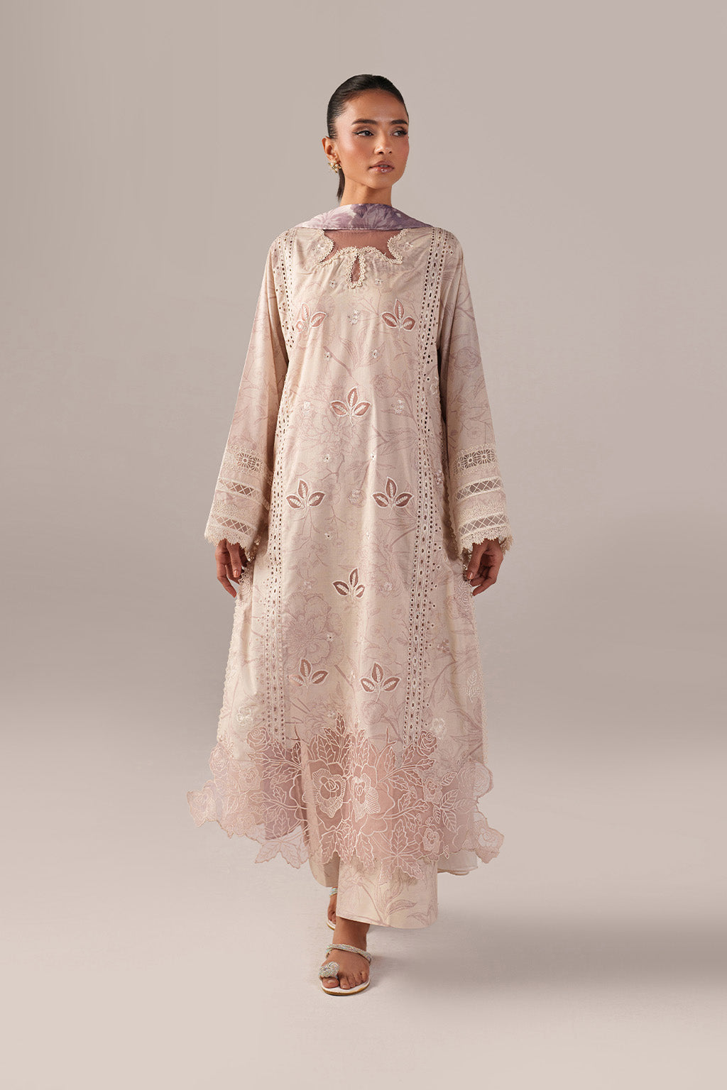 Woman wearing a long, light pink embroidered dress against a neutral background