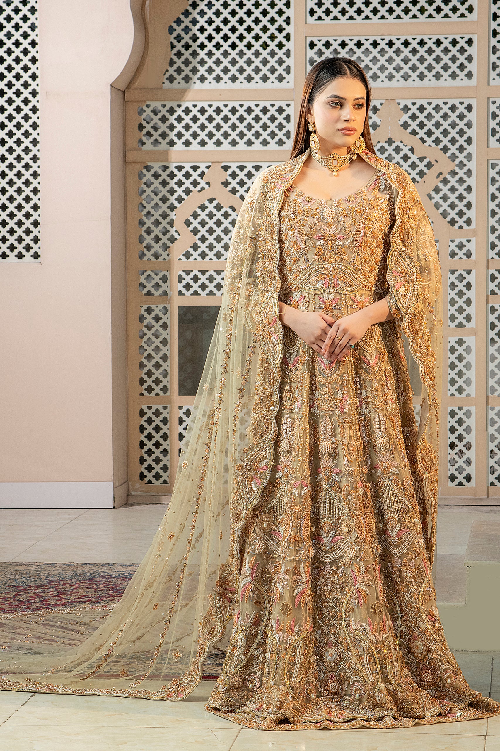 A woman wearing a traditional, fawn-colored maxi dress with embroidery and a dupatta (overlay) featuring an all-over jaal pattern and elaborate embroidery.