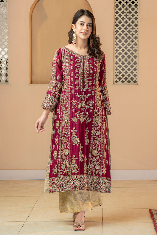 A woman wearing a traditional, vibrant red and gold silk dress with a dupatta, standing in a room with a reflective floor and decorative walls.
