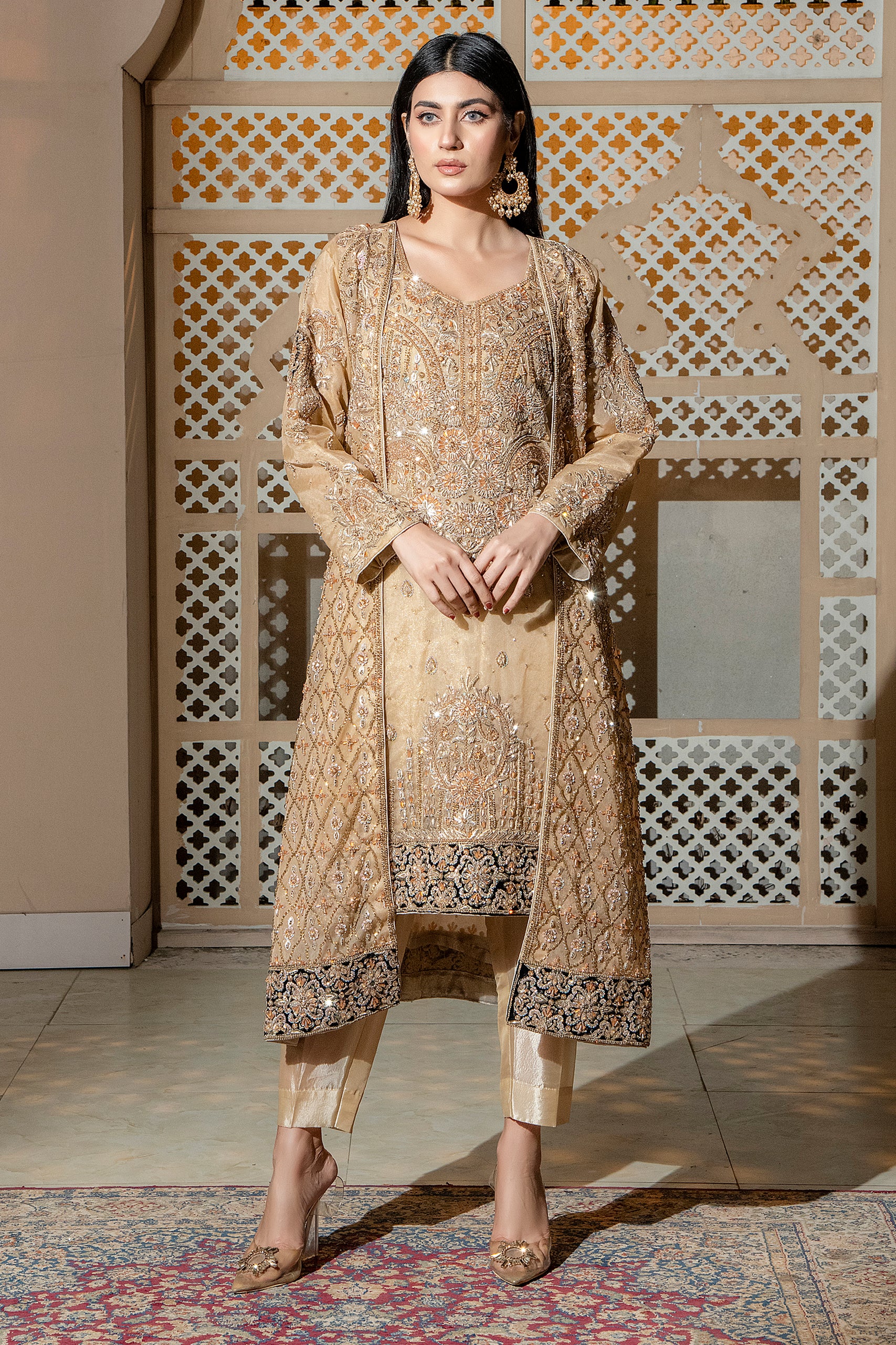 A woman standing in a traditional, elegant attire with a golden organza fabric, featuring embellishments such as crystals and possibly kundans.