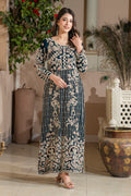 A woman wearing a traditional, embroidered, sea green velvet dress with a dupatta, standing in a room with decorative plants and furniture.