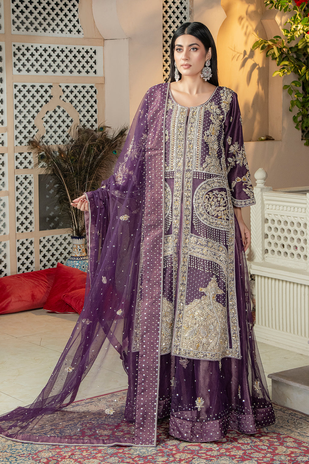A woman wearing a traditional purple lehenga with intricate embroidery and a shimmering fabric, posed elegantly against a backdrop with geometric patterns.
