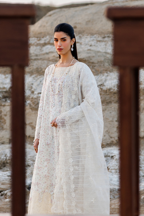 Woman in a white traditional outfit standing against a textured wall.