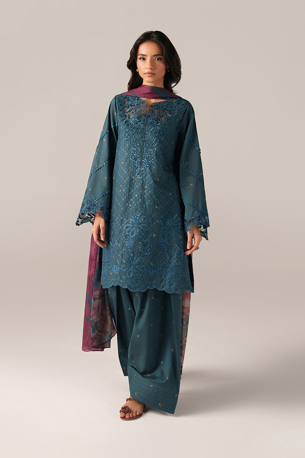 Woman wearing a teal embroidered outfit with a plain background