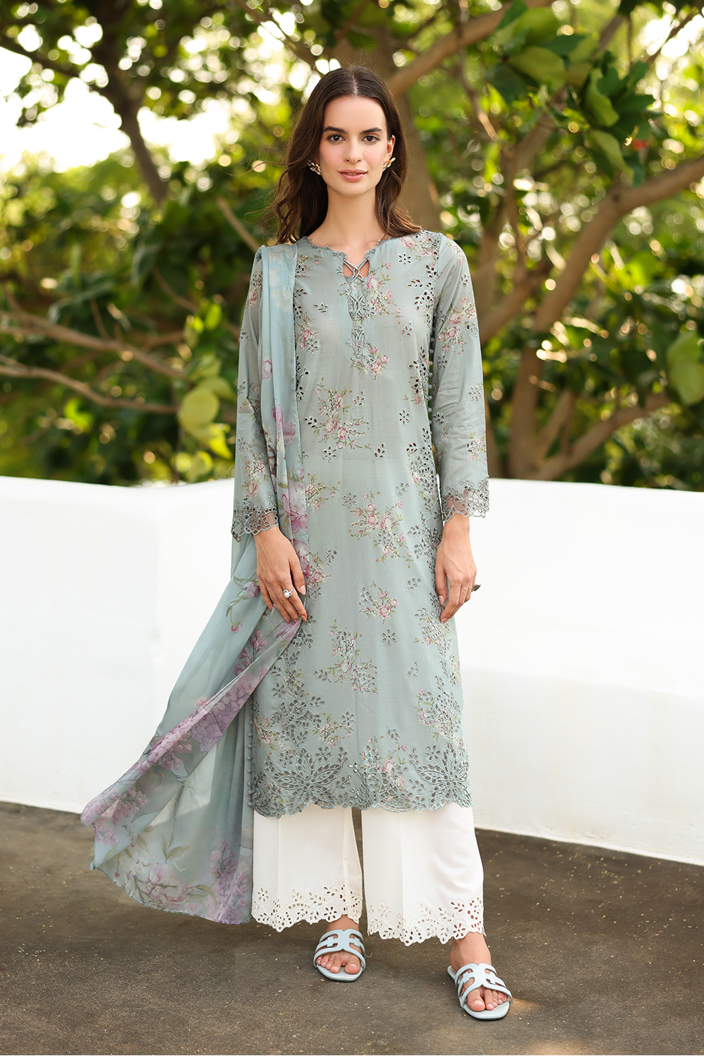 Woman wearing a light blue embroidered kurta with white pants and a dupatta, standing outdoors.