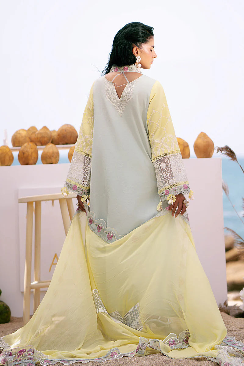 Woman in a light yellow and white traditional outfit with floral patterns, standing against a blurred outdoor background.