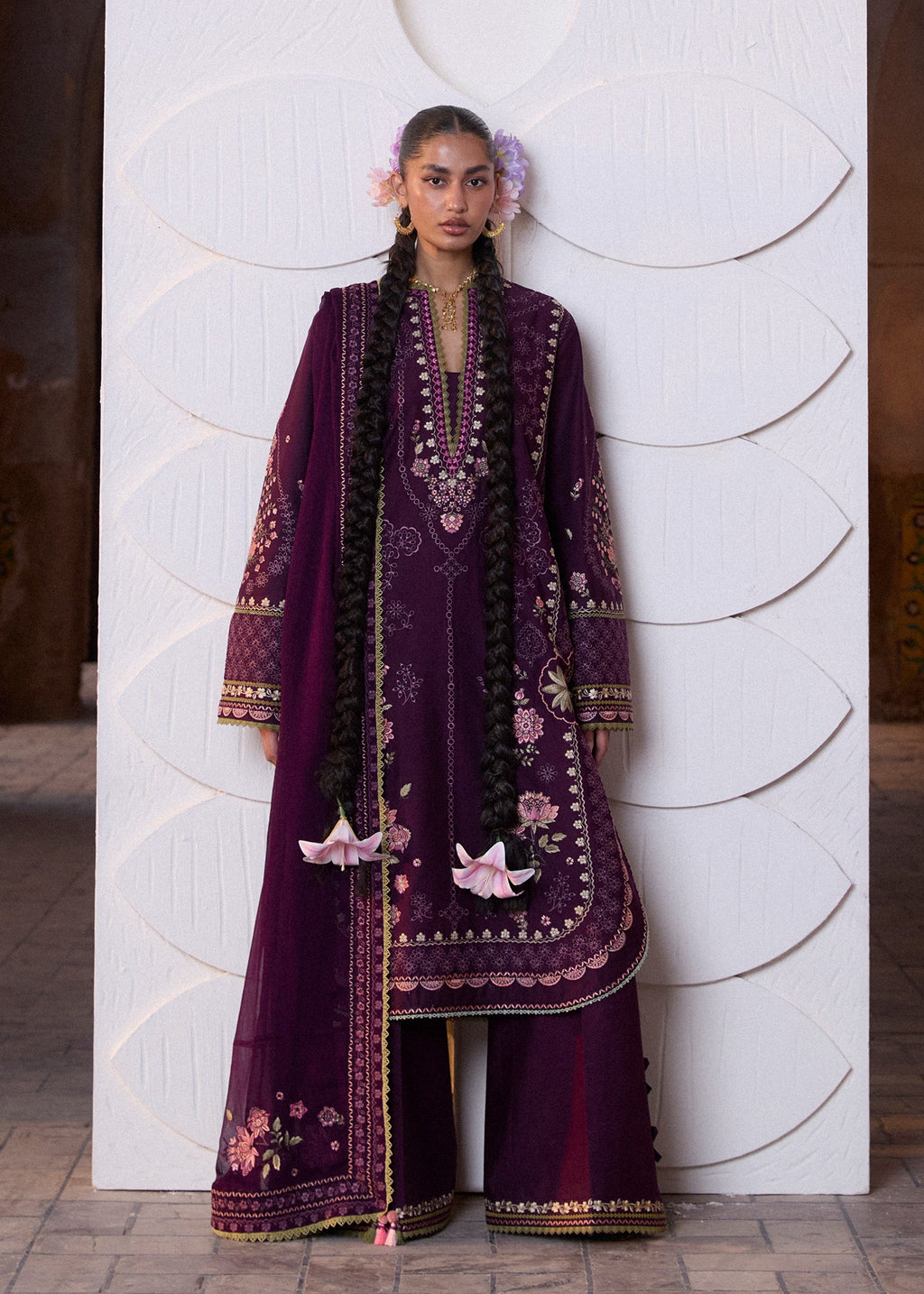 Woman wearing a traditional embroidered outfit against a white wall.