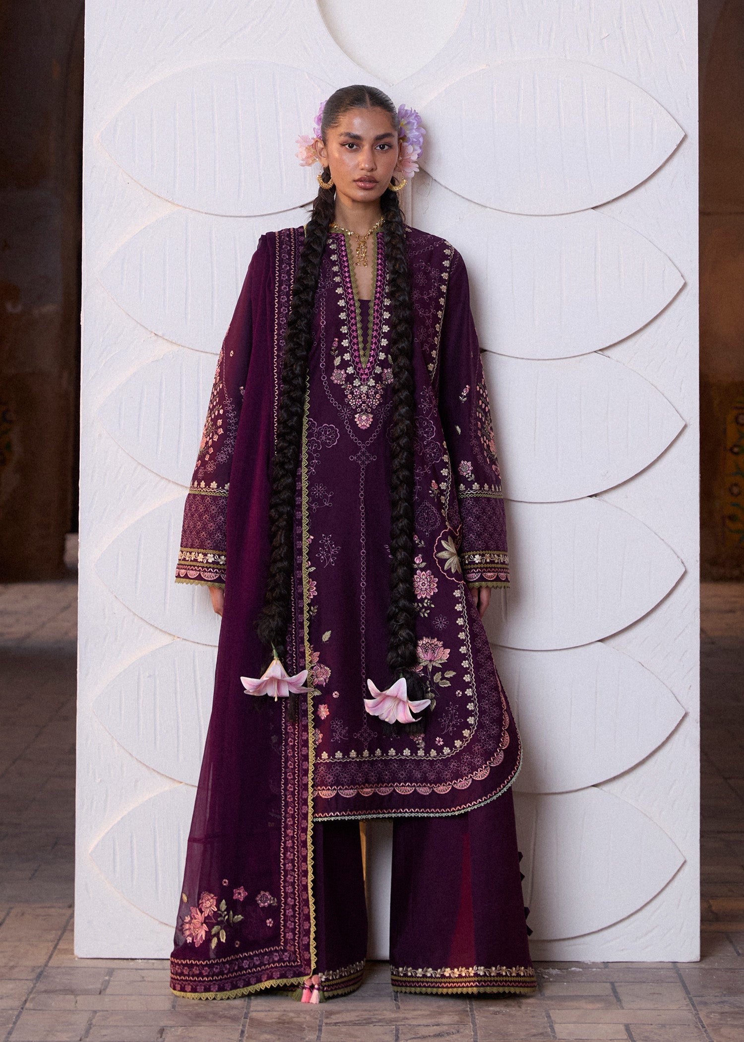 Woman wearing a traditional embroidered outfit against a white wall.