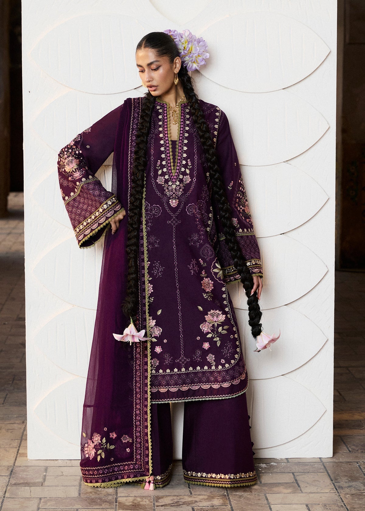Woman wearing a purple embroidered traditional outfit against a white wall.
