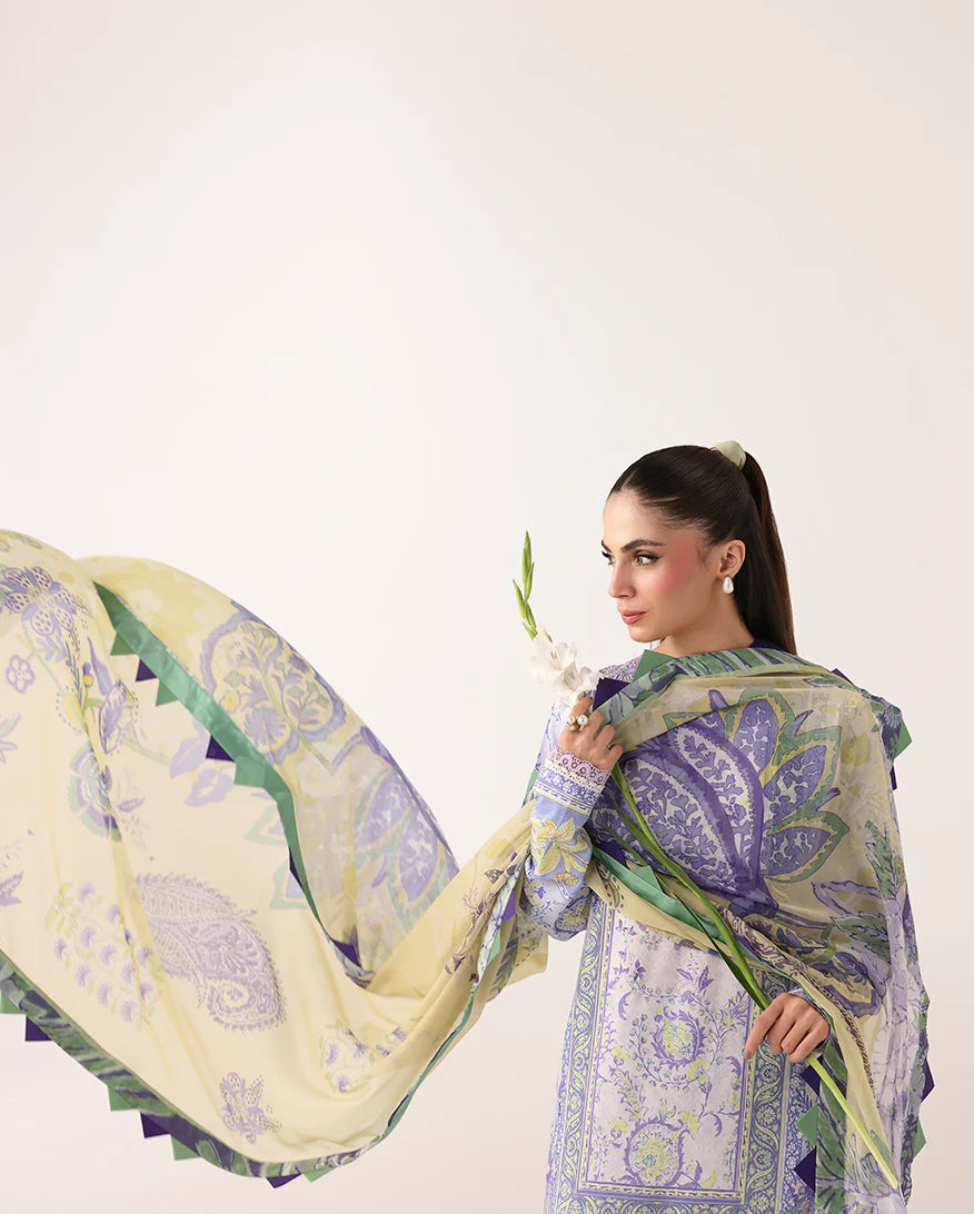 Woman wearing a patterned outfit with a large scarf, holding flowers against a white background
