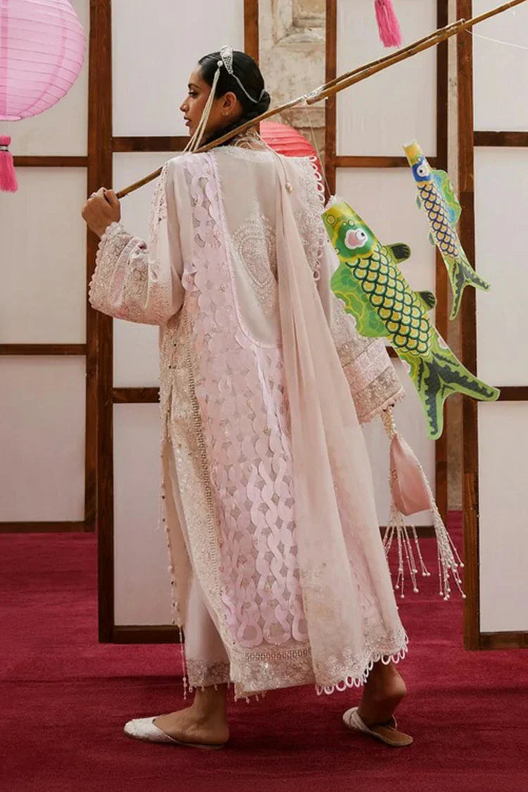 Person in a traditional outfit holding a broom with decorative fish attached, against a wooden panel background.