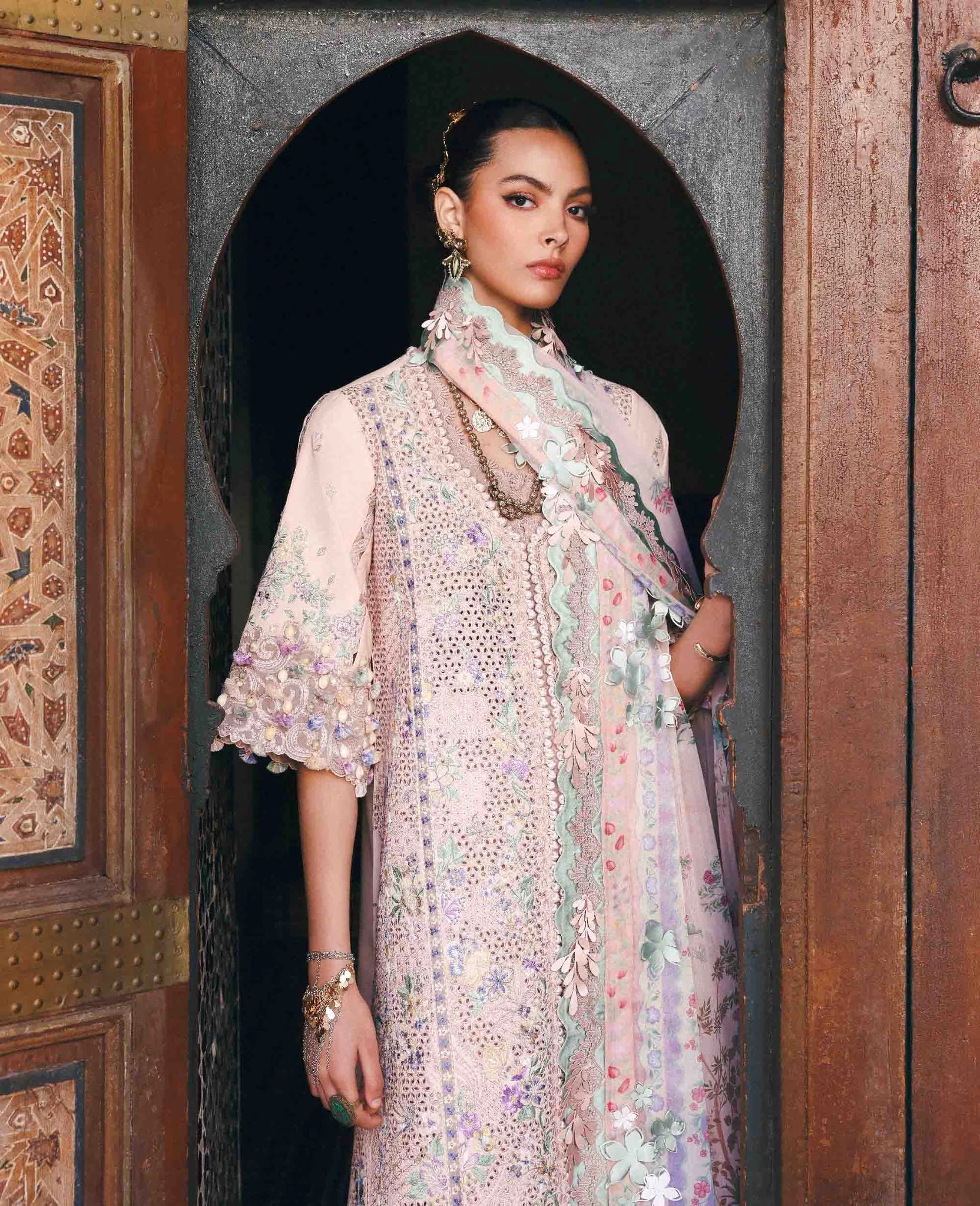 Woman in a floral outfit standing in front of an ornate wooden door.