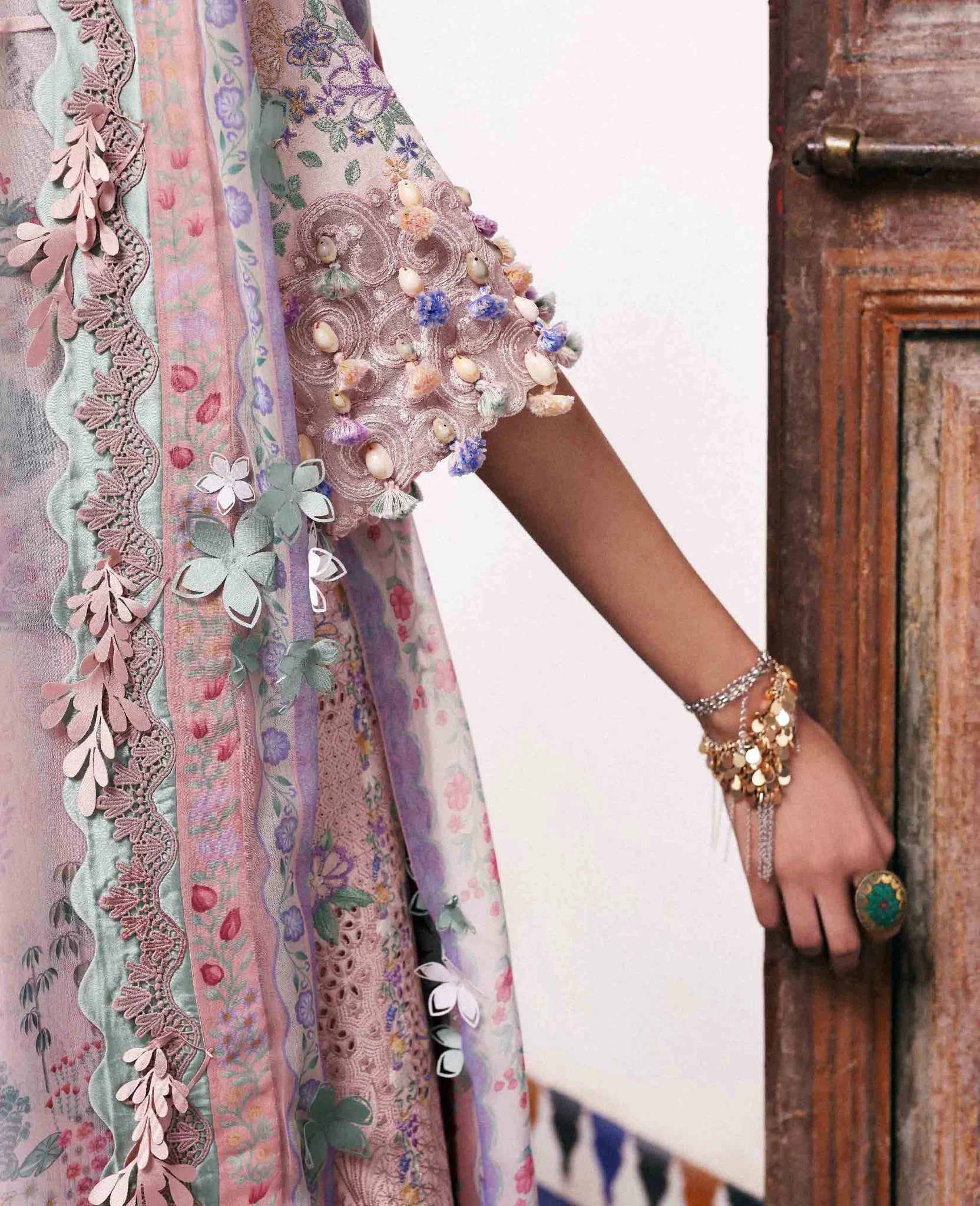 Close-up of a person wearing a colorful embroidered garment with floral patterns, standing against a wooden door.