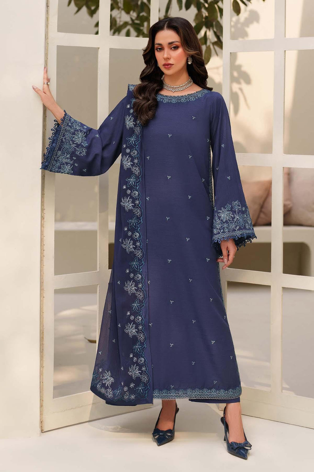 Woman wearing a blue embroidered dress with a matching jacket indoors.