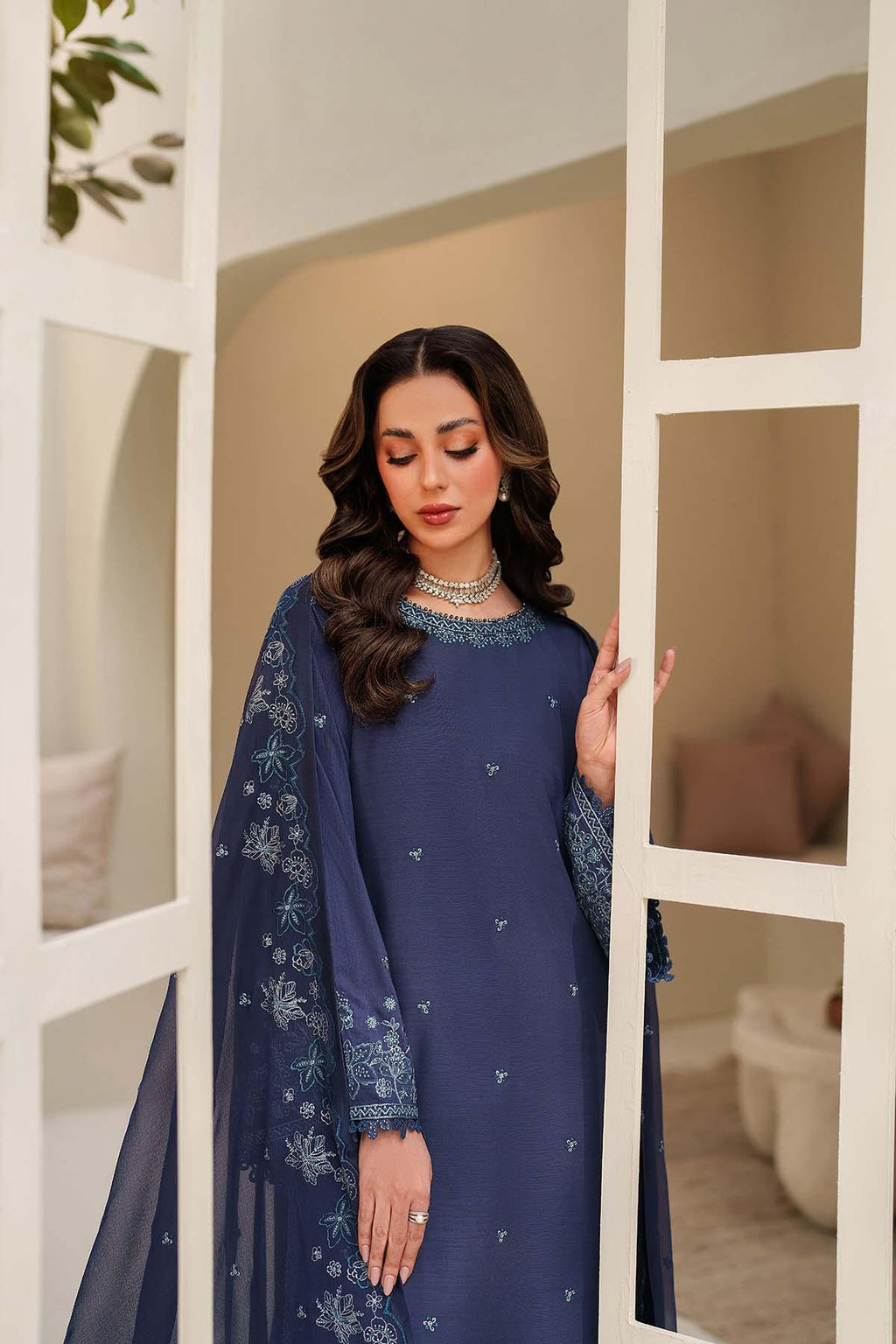 Woman wearing a blue embroidered dress standing in front of a mirror.