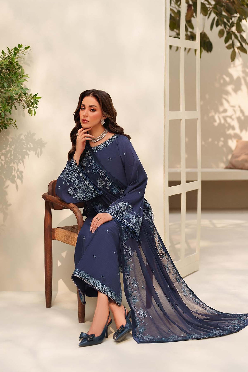 Woman in a blue embroidered outfit sitting on a chair with a white background