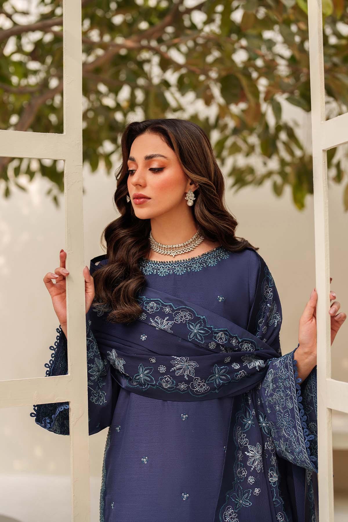 Woman in a blue embroidered outfit standing against a white lattice background