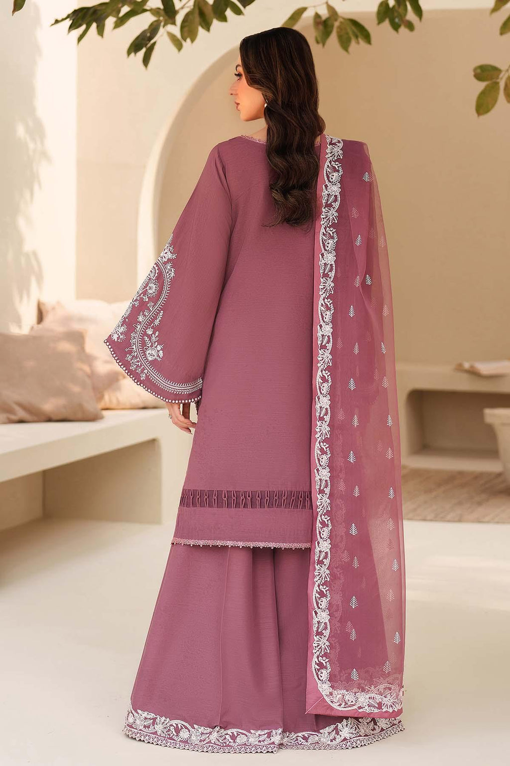Woman wearing a mauve traditional outfit with white embroidery in an indoor setting.