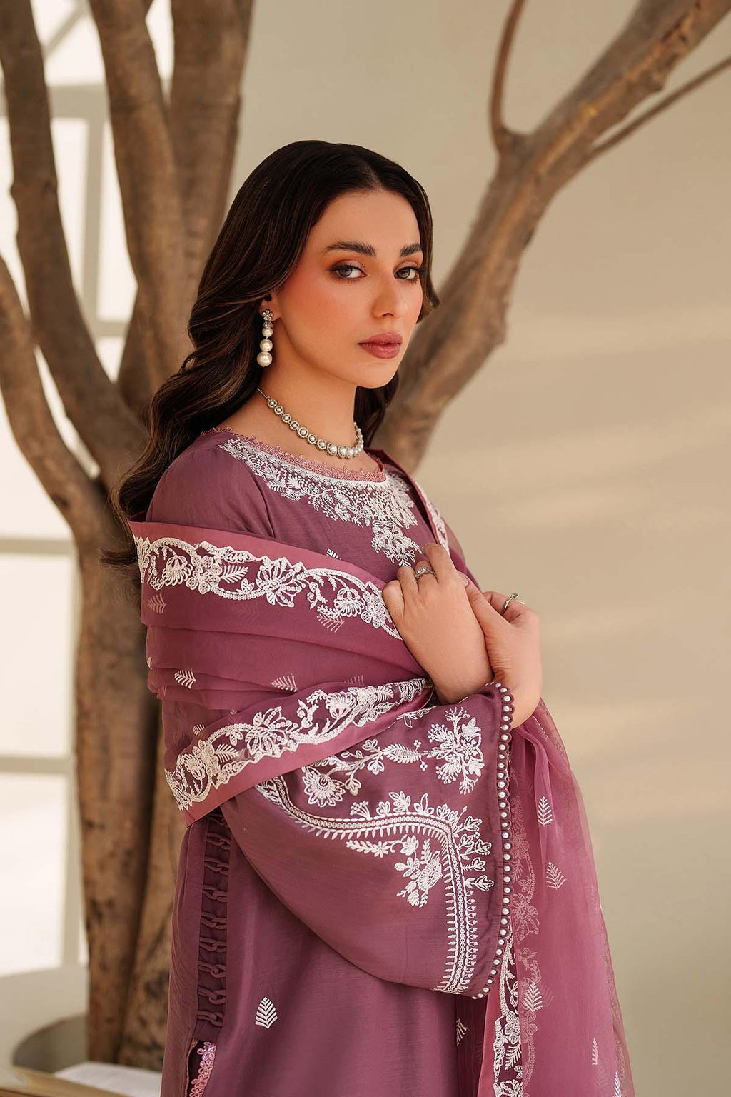 Woman wearing a purple saree with white embroidery standing against a neutral background.