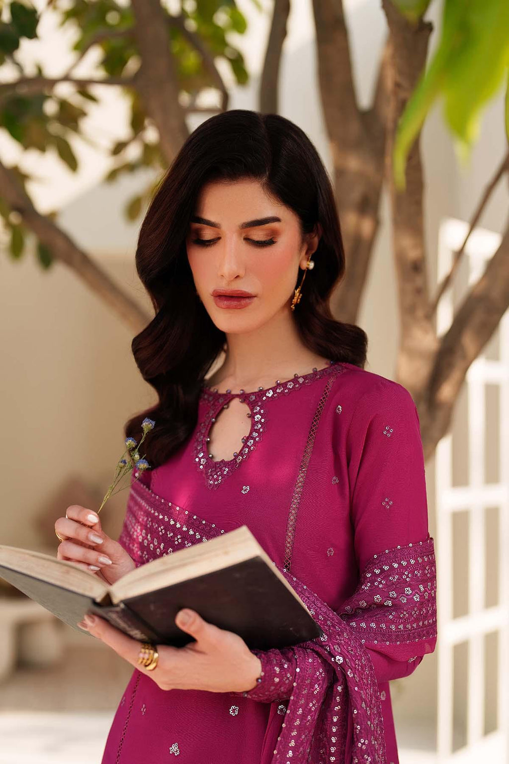 Woman in a purple traditional outfit reading a book outdoors.