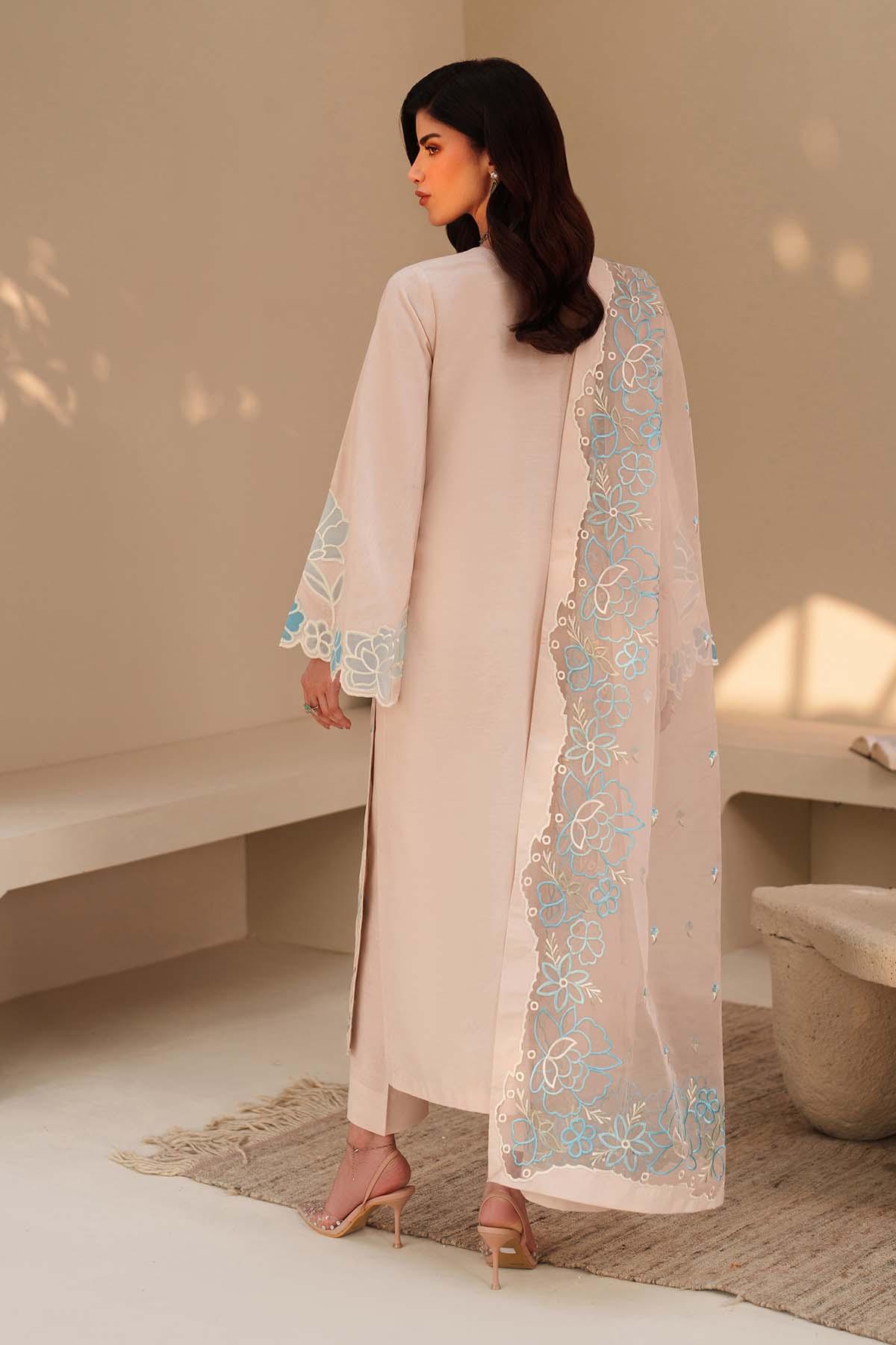 Woman wearing a light pink outfit with floral embroidery in a minimalistic setting
