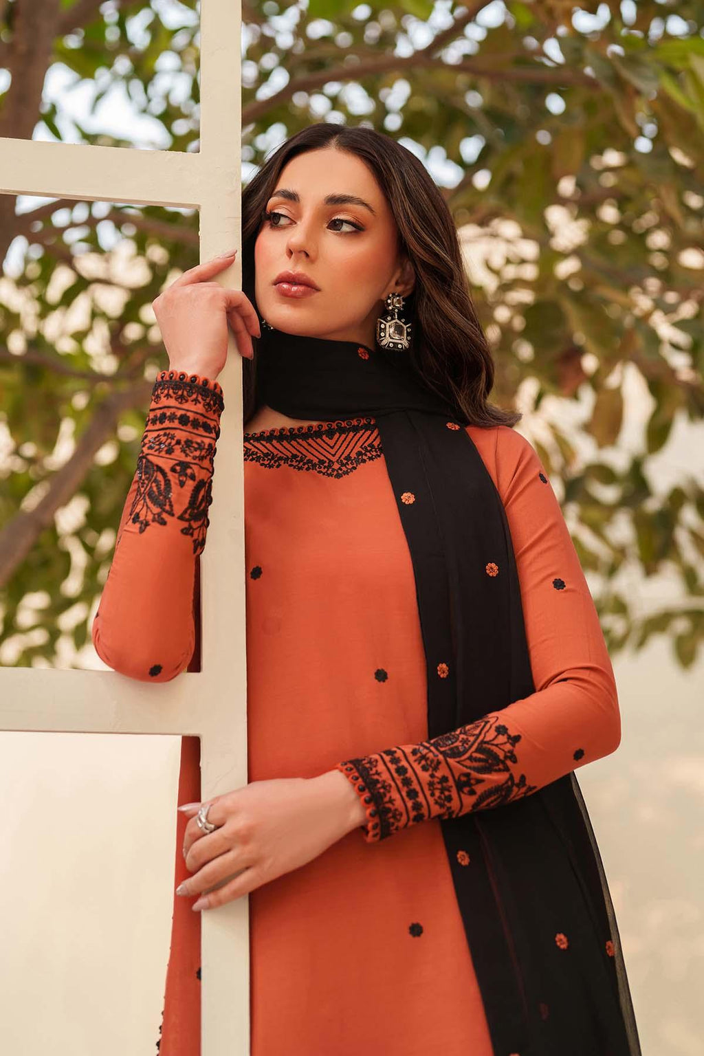 Woman wearing an orange and black outfit with intricate patterns, standing outdoors.