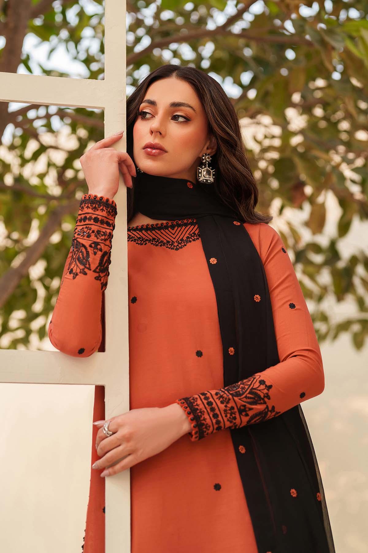 Woman wearing an orange and black outfit with intricate patterns, standing outdoors.