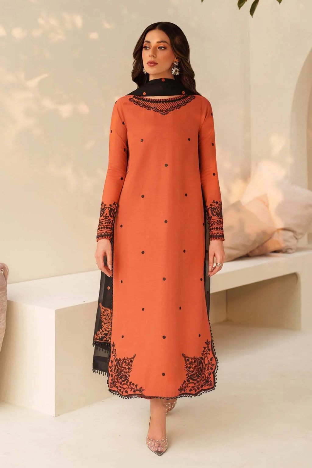 Woman wearing an orange dress with black lace details in a minimalistic setting.