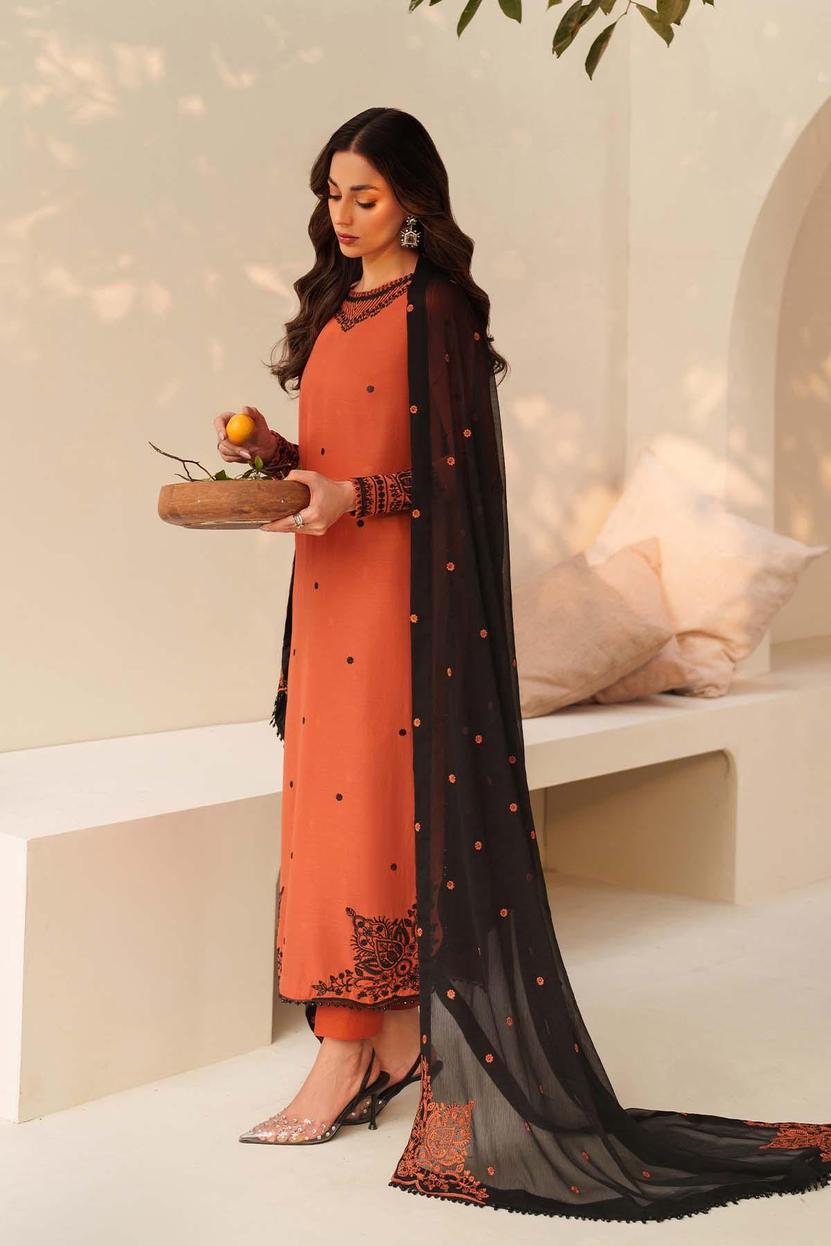 Woman in an orange kurta with black dupatta holding a basket of flowers indoors.