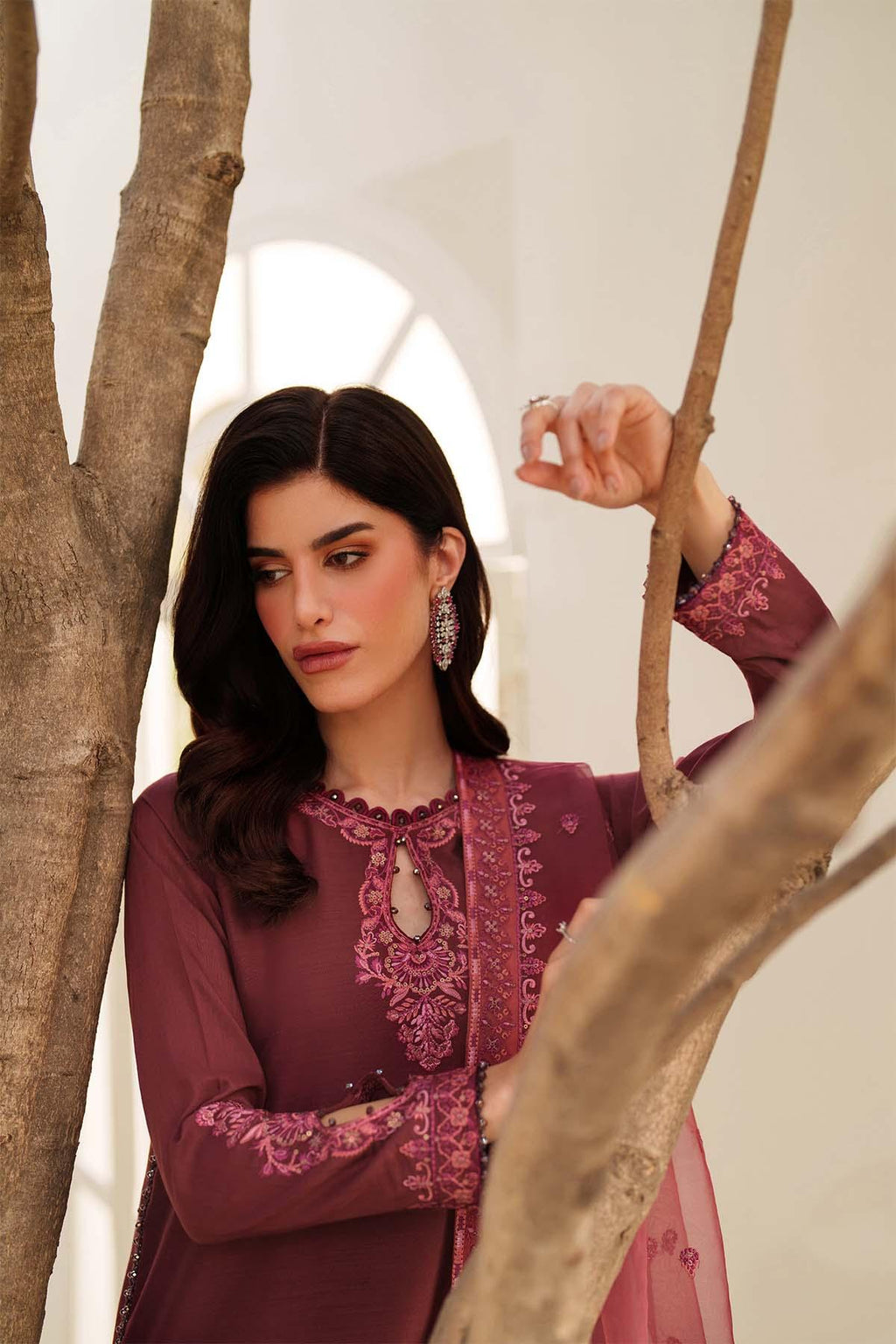 Woman in a maroon embroidered outfit standing among trees with a white tent in the background