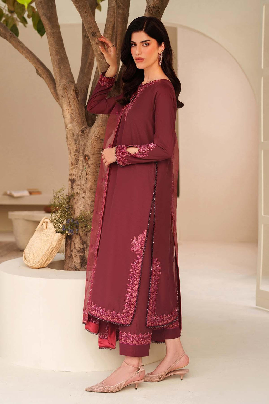 Woman in a maroon traditional outfit with floral patterns standing indoors.