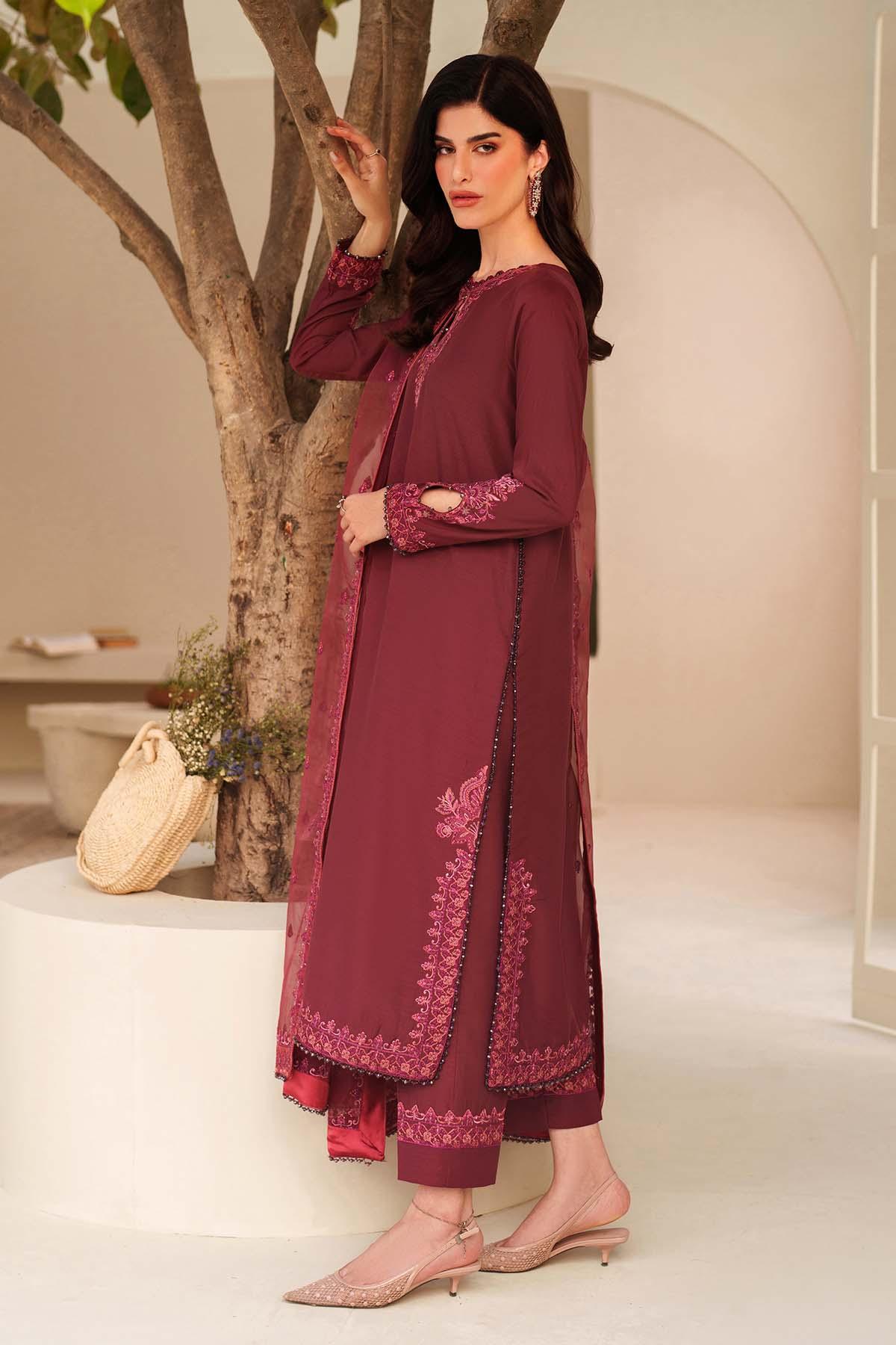 Woman in a maroon traditional outfit with floral patterns standing indoors.