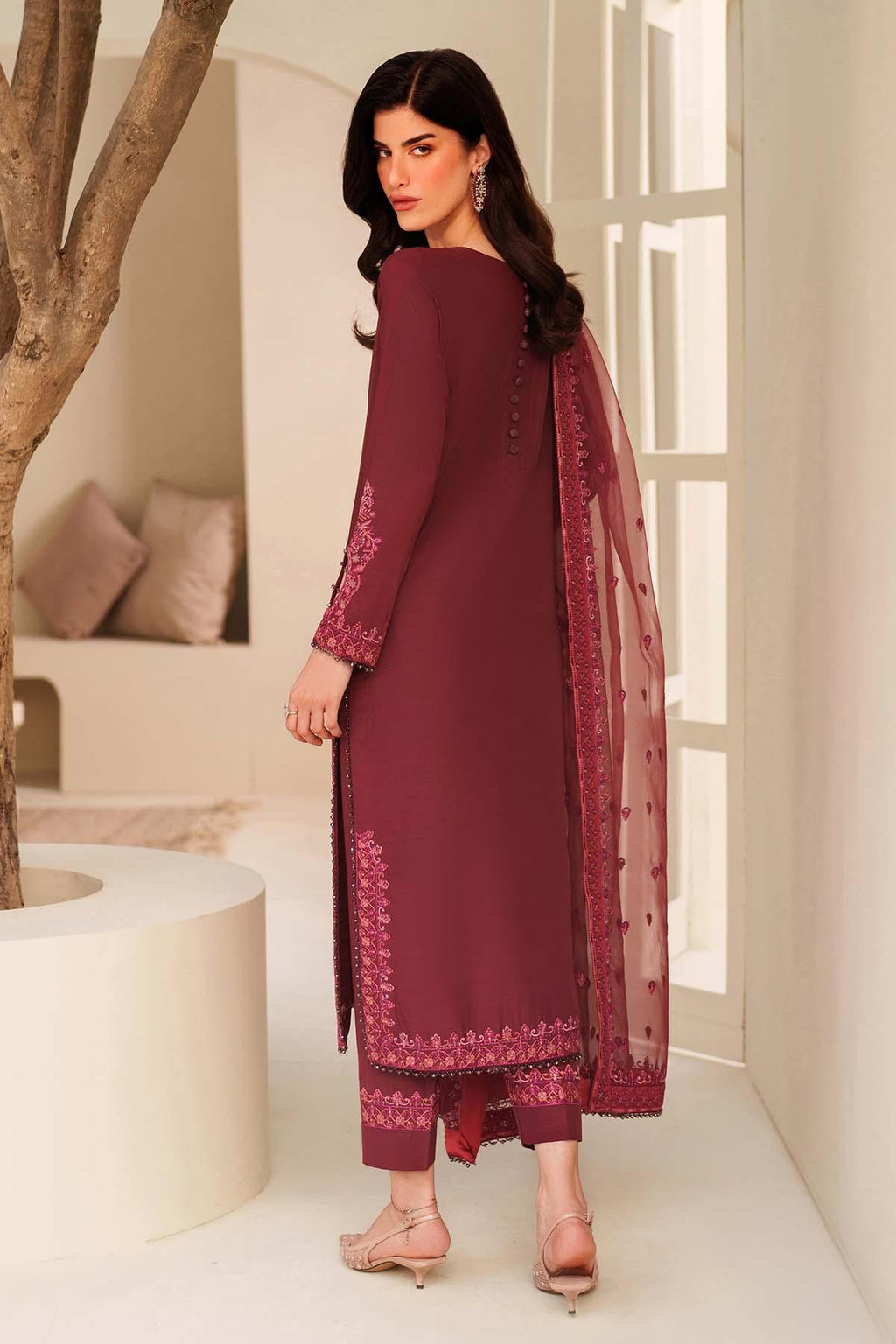 Woman in a maroon traditional outfit with a sheer dupatta in a minimalistic indoor setting.