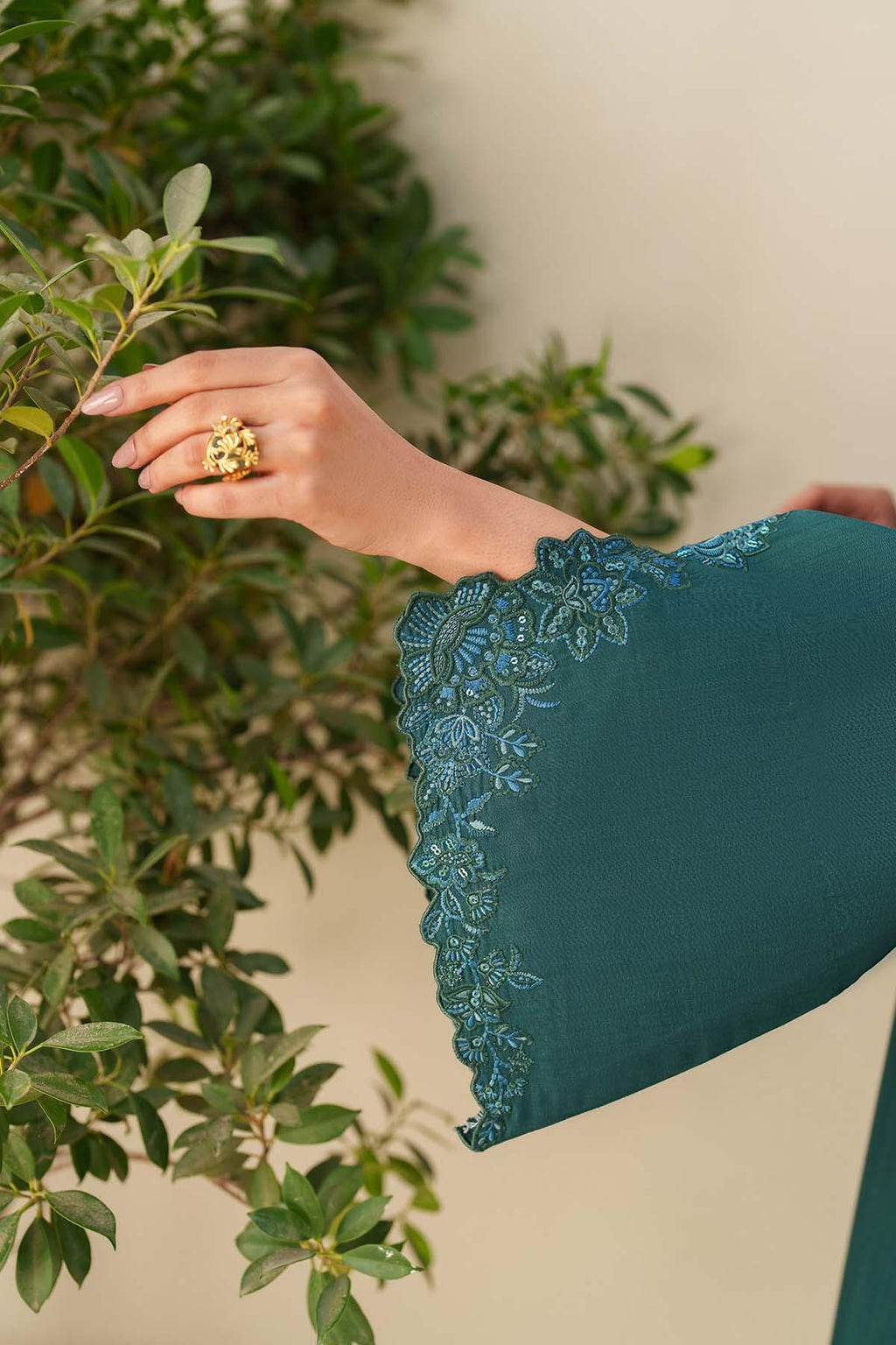 Teal lace-trimmed garment with a hand wearing a gold ring against a green leafy background
