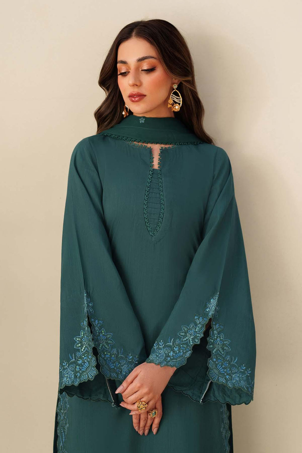 Woman wearing a teal dress with intricate lace details against a beige background
