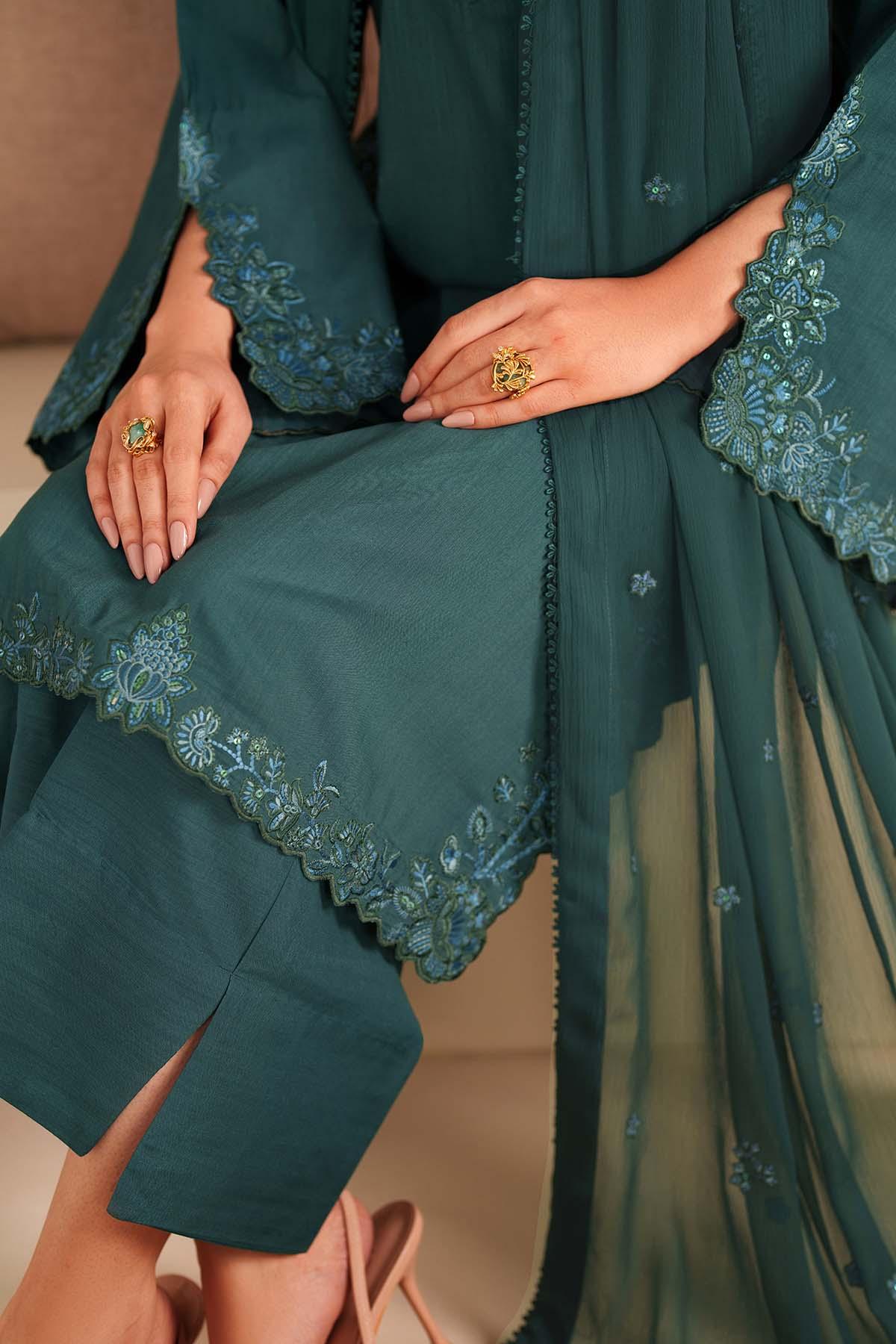 Teal embroidered outfit with close-up of hands wearing rings.