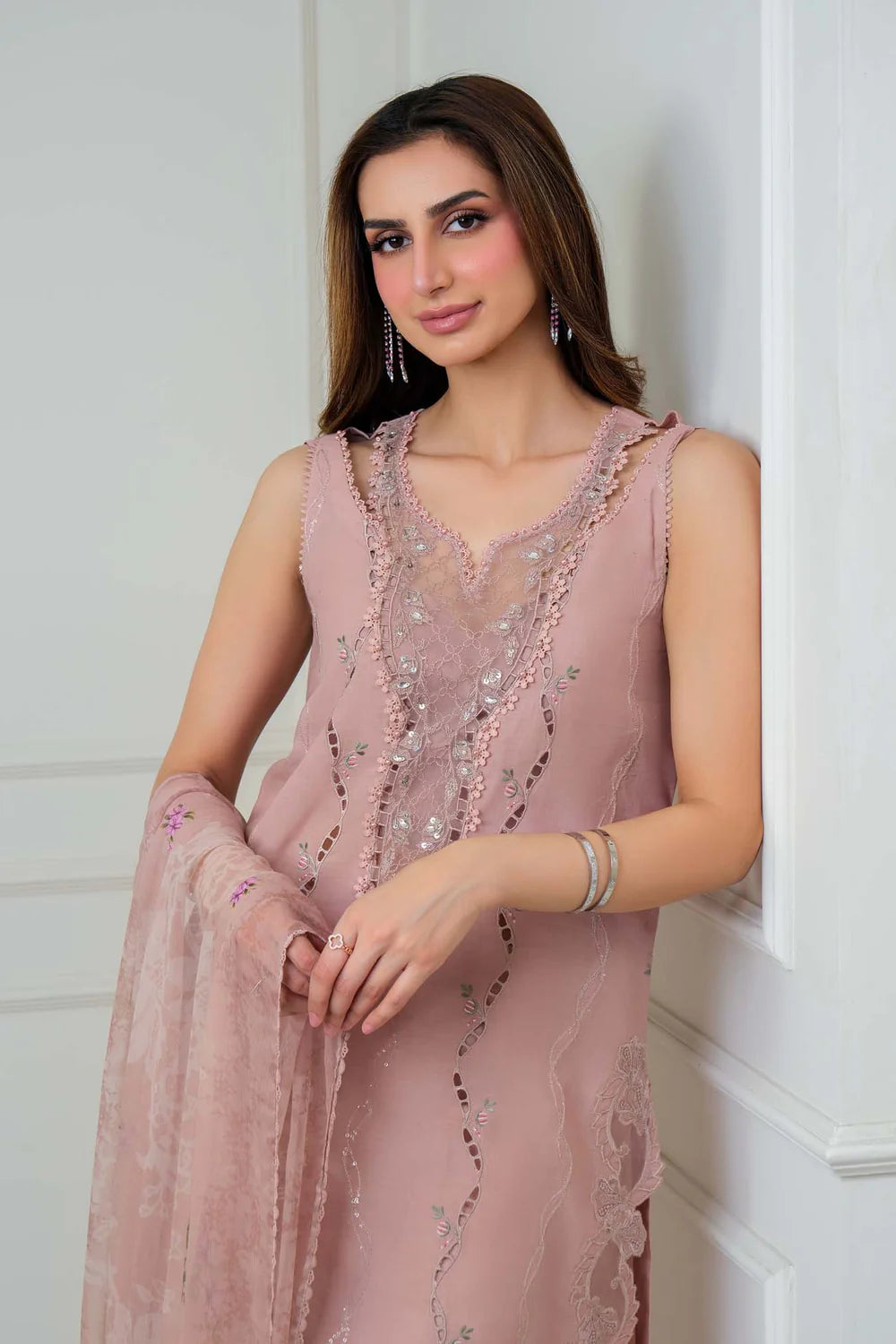 Woman wearing a pink embroidered dress against a white wall