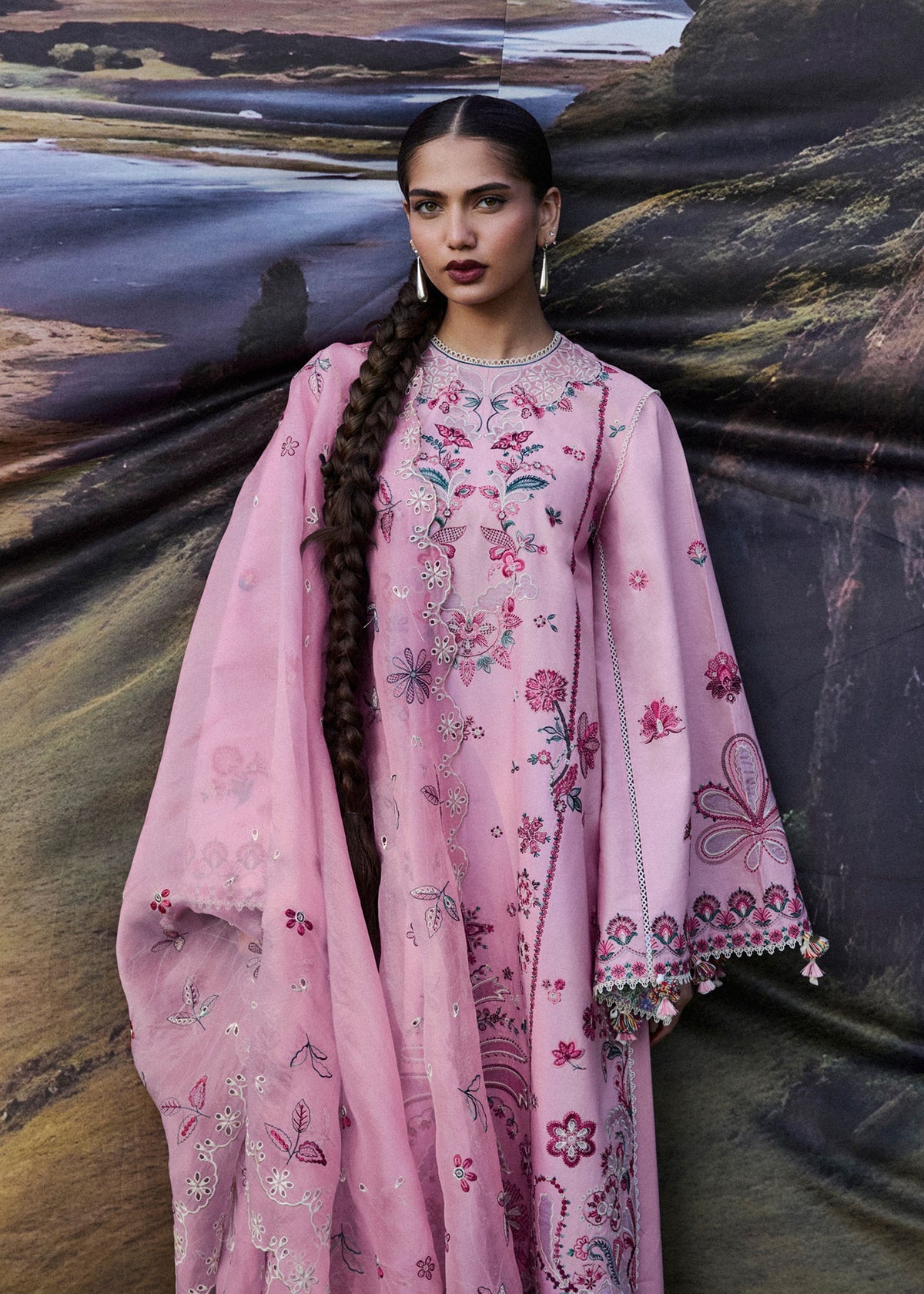 Woman in a pink embroidered outfit standing against a scenic background