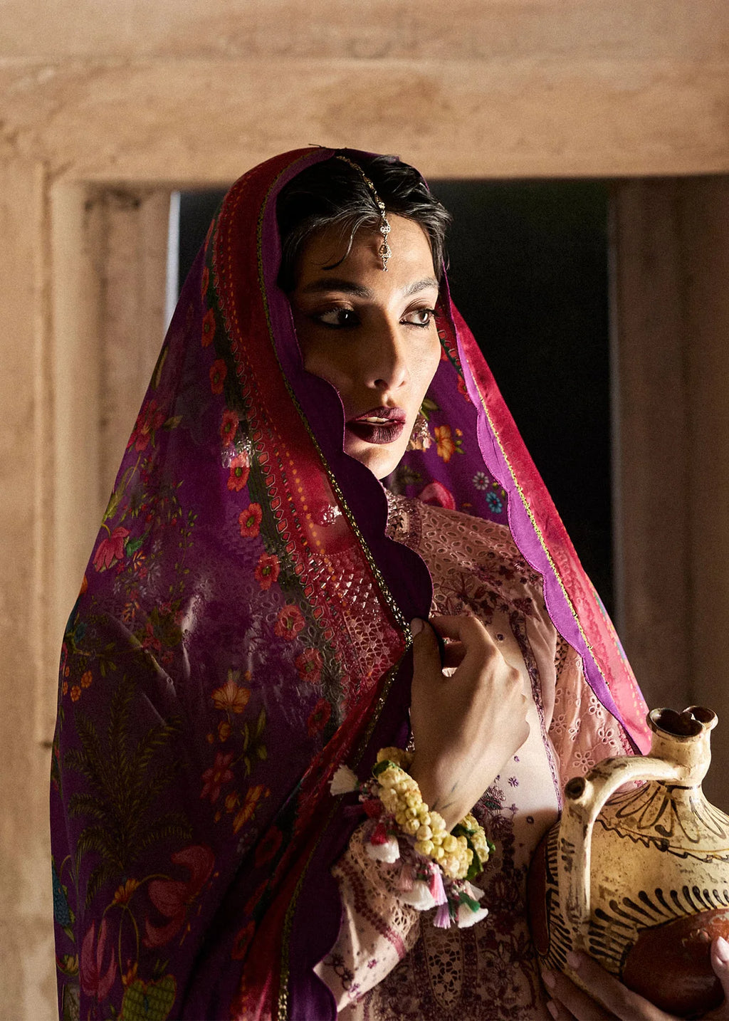 Woman in traditional attire holding a ceramic pot indoors.