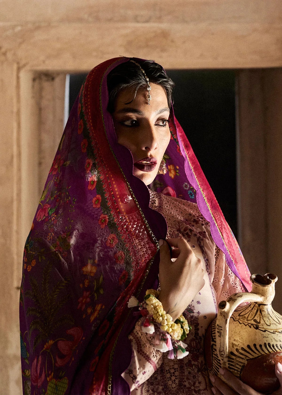 Woman in traditional attire holding a ceramic pot indoors.