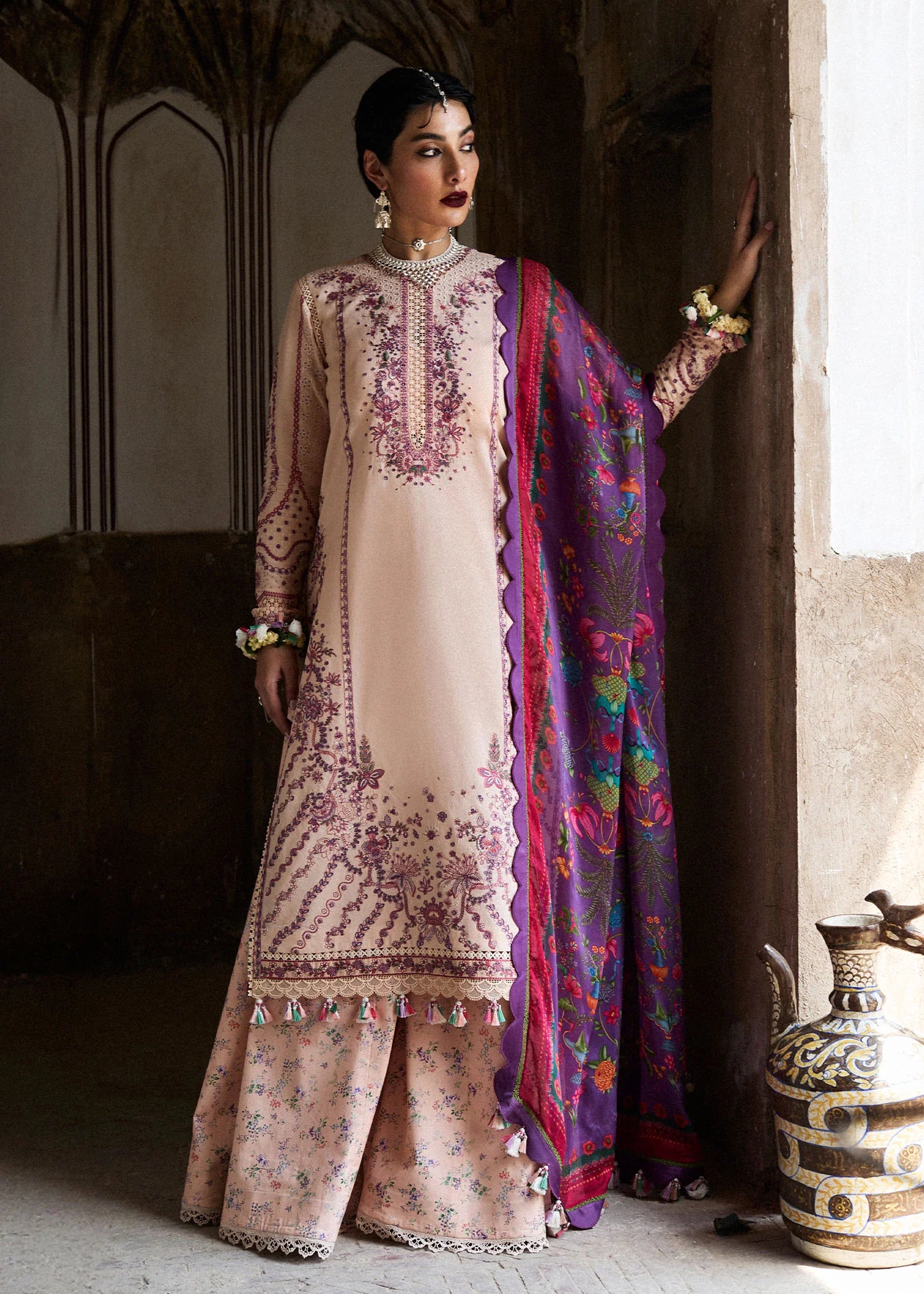 Woman in traditional outfit with embroidered top and colorful dupatta standing indoors.