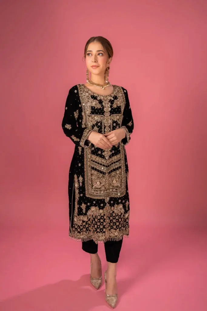 Woman wearing a black and gold embroidered dress against a pink background