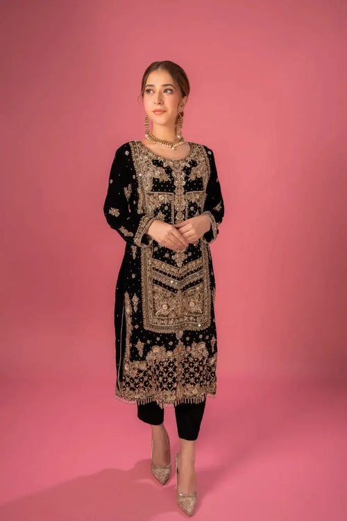 Woman wearing a black and gold embroidered dress against a pink background