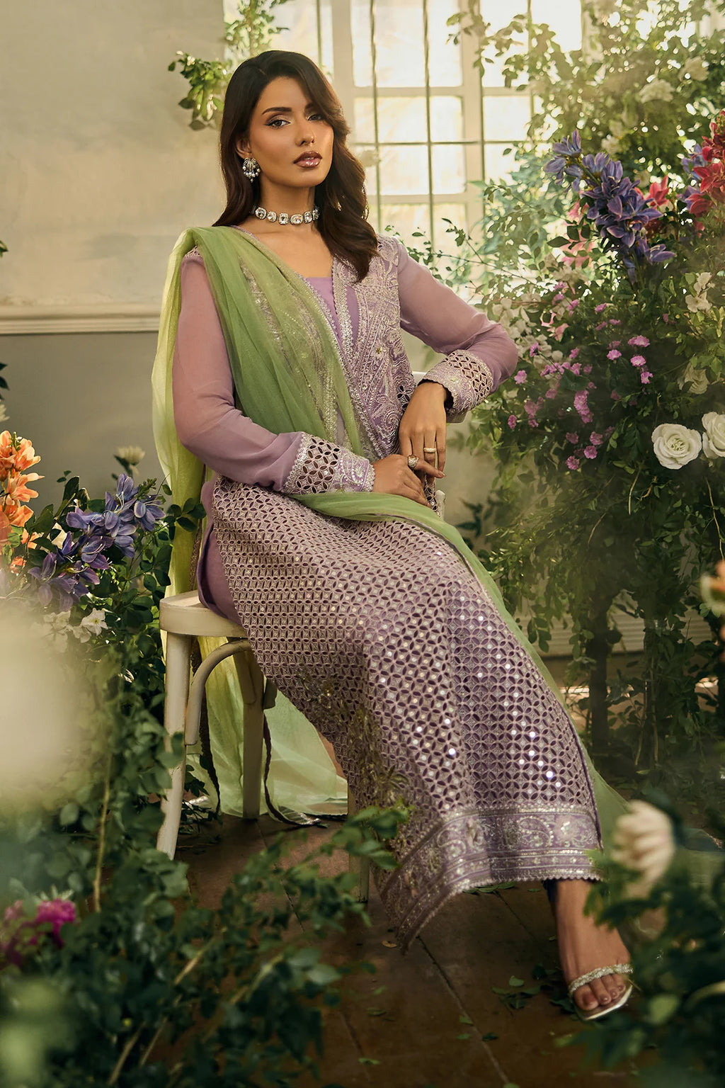 Woman in a purple and green traditional outfit sitting among flowers