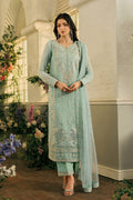 Woman in a light blue embroidered traditional outfit standing in a decorative indoor setting with flowers.