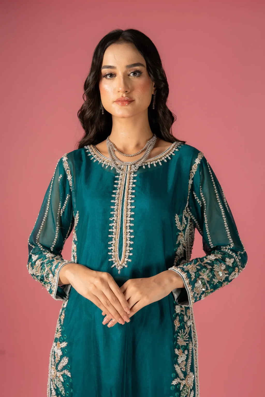 A woman wearing a traditional, dark sea green, embroidered dress with a floral design, paired with a dupatta and a shirt.